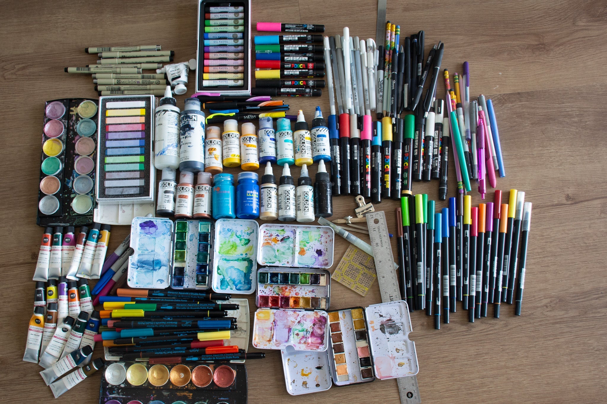 Flat lay of essential art supplies including watercolor palettes, Golden acrylics, pens, markers, brushes, and rulers — artist's toolkit for moving abroad.